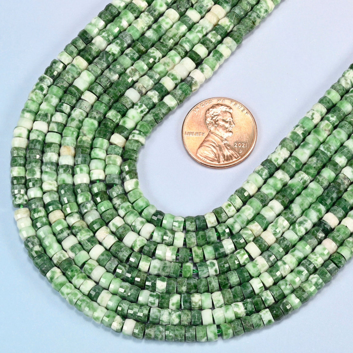 Close view of tree agate faceted heishi disc strands curving beside a US penny for scale