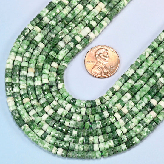 Close view of tree agate faceted heishi disc strands curving beside a US penny for scale
