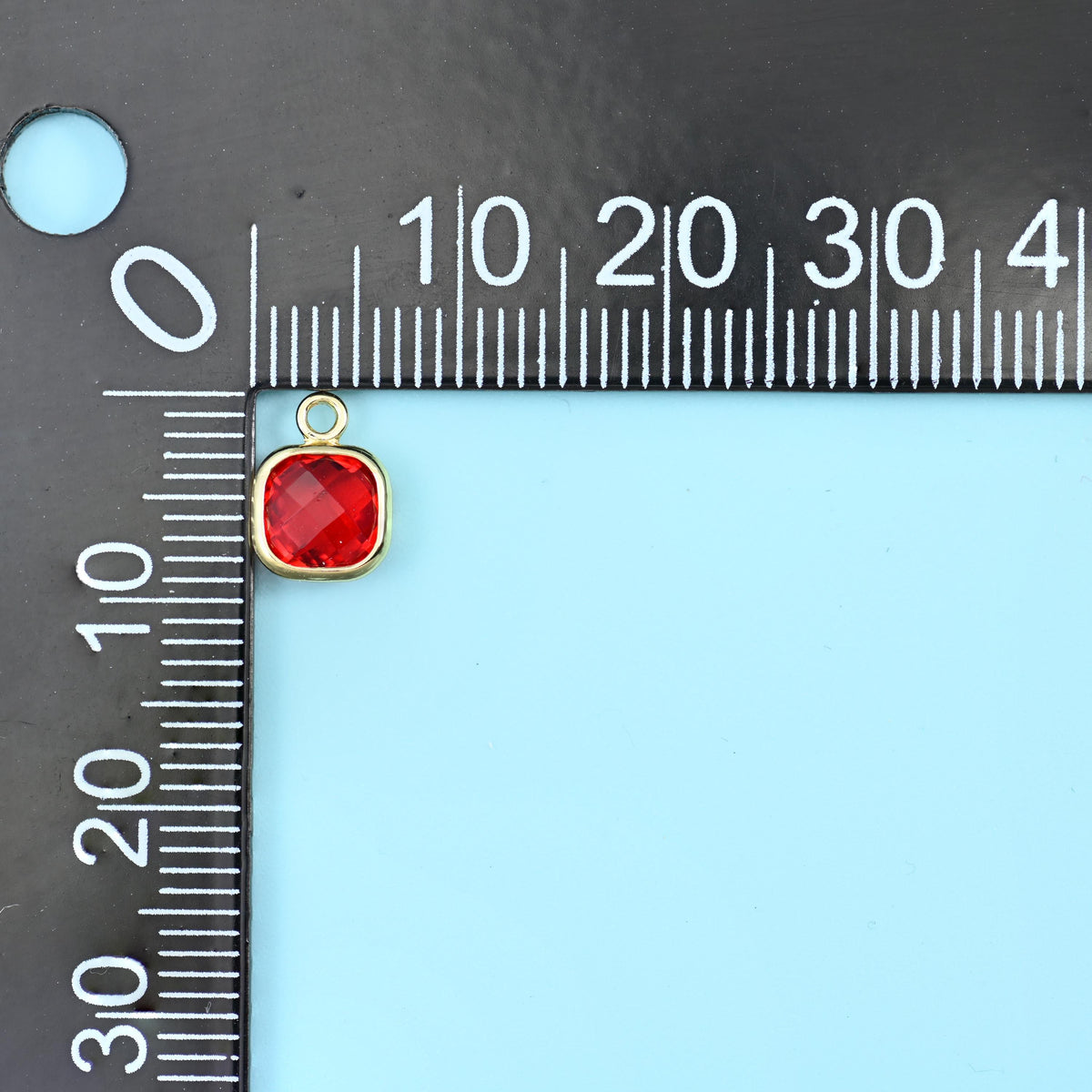 Faceted square zirconia charm in red on a black millimetre ruler, about 9mm across.
