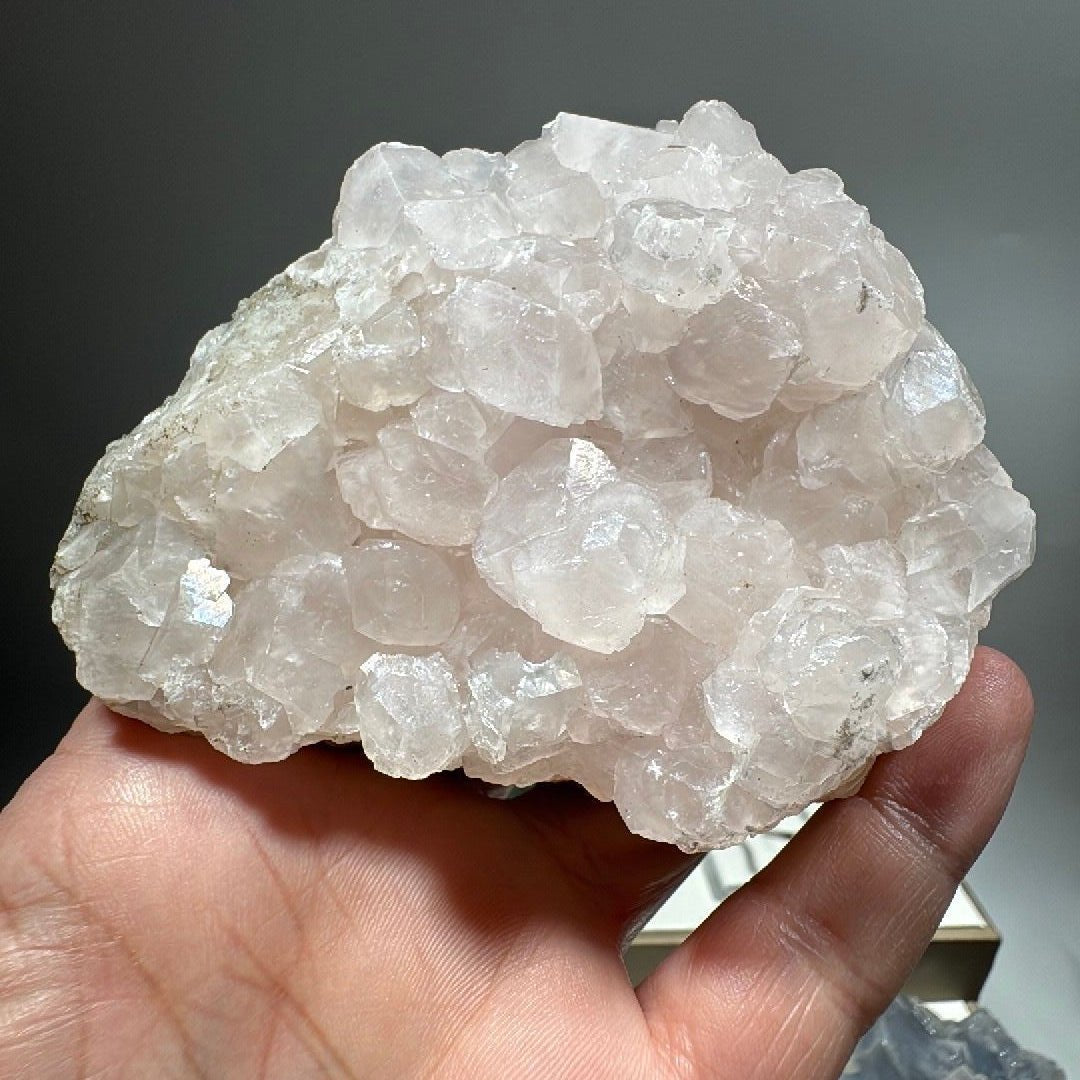 Pink calcite crystal cluster held in an open hand, creamy white blocky crystals