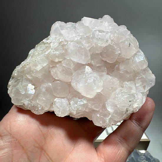 Pink calcite crystal cluster held in an open hand, creamy white blocky crystals