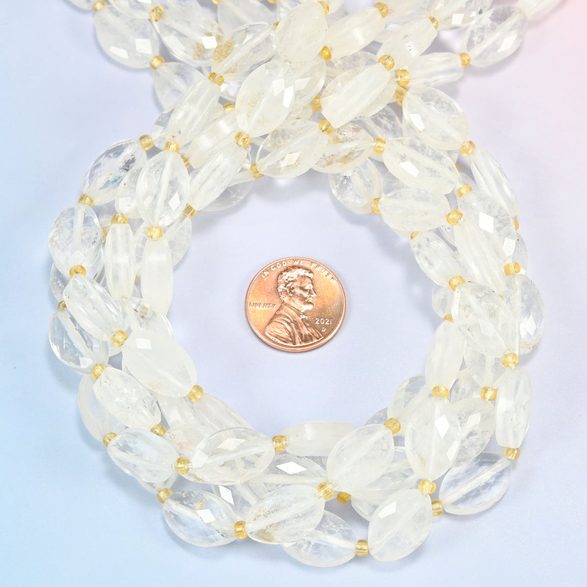 Clear quartz faceted flat oval beads 9x14mm coiled in a loop around a US penny for scale, close-up of the faceted flat oval shape
