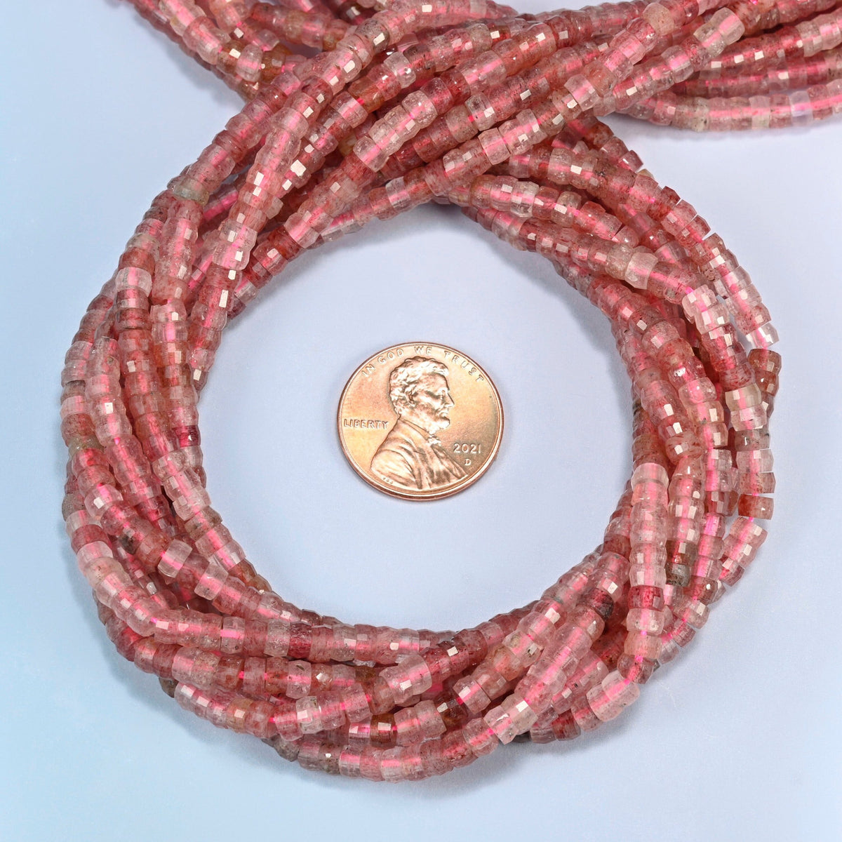 Strawberry quartz faceted heishi disc beads 2x4mm coiled in a loop around a US penny for scale, close-up of the faceted disc shape