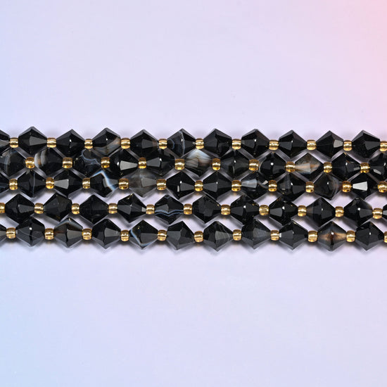 Dyed black strip agate bicone beads in straight rows, seen close up, each bead cut to two points meeting at a wide center, facets catching hard highlights.