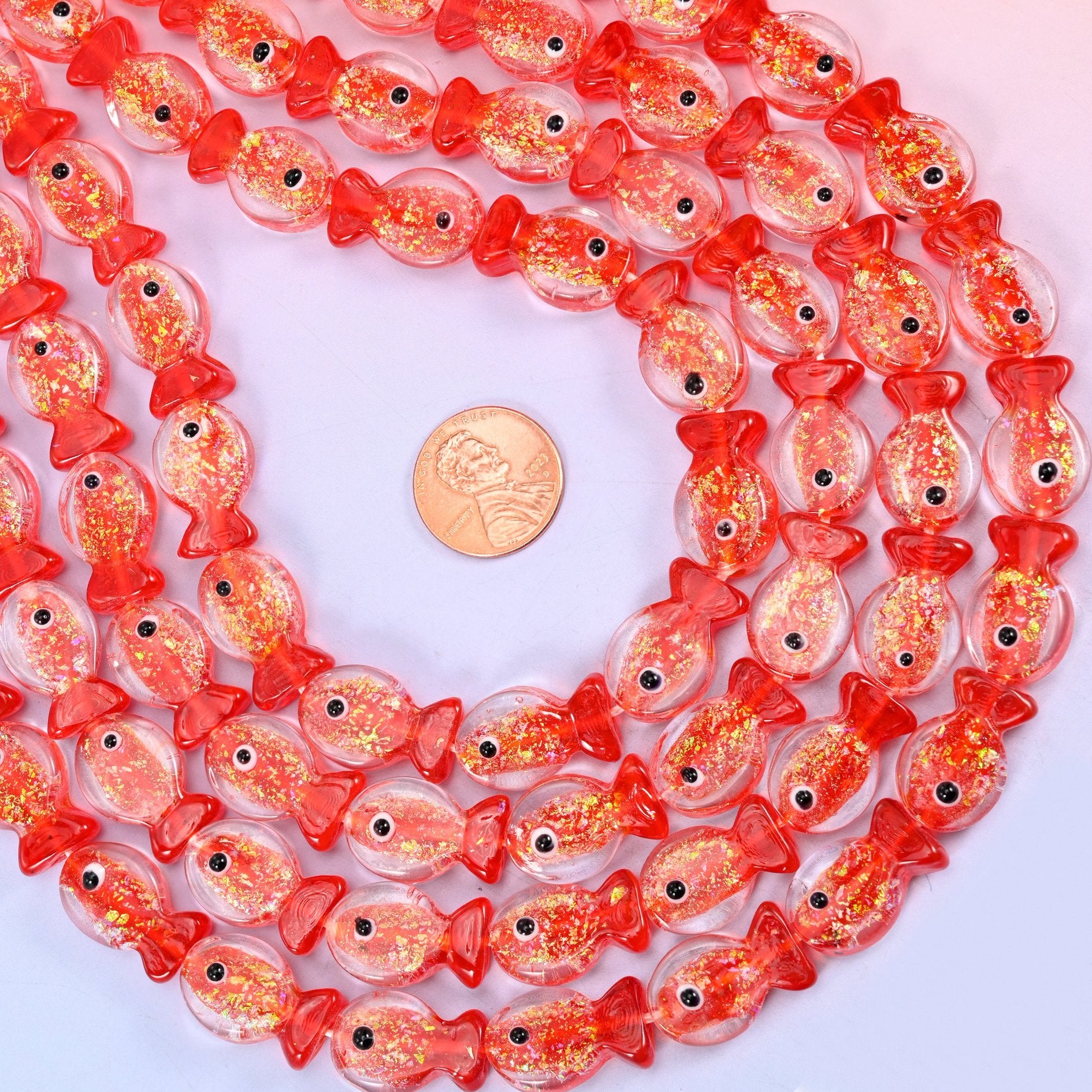 Red Fish Glass Beads — clear glass fish washed with coral red at the head and tail and shot through with gold glitter flecks, each finished with a hand-painted black and white eye.