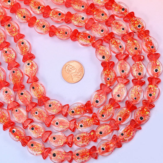 Red Fish Glass Beads — clear glass fish washed with coral red at the head and tail and shot through with gold glitter flecks, each finished with a hand-painted black and white eye.