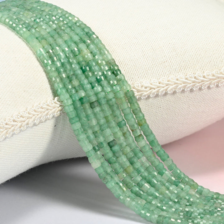 Green aventurine faceted heishi disc beads 2x4mm, several strands draped over a white cushion
