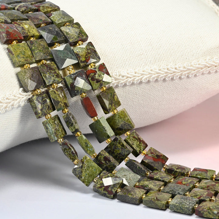 Natural dragon blood stone faceted flat square beads 10x10mm with small gold seed bead spacers, several strands draped over a white cushion