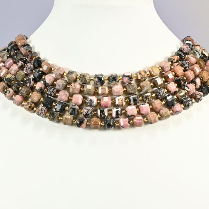 Rhodonite faceted cube strands layered as a collar on a white display bust, pink and peach cubes alternating with black veined ones