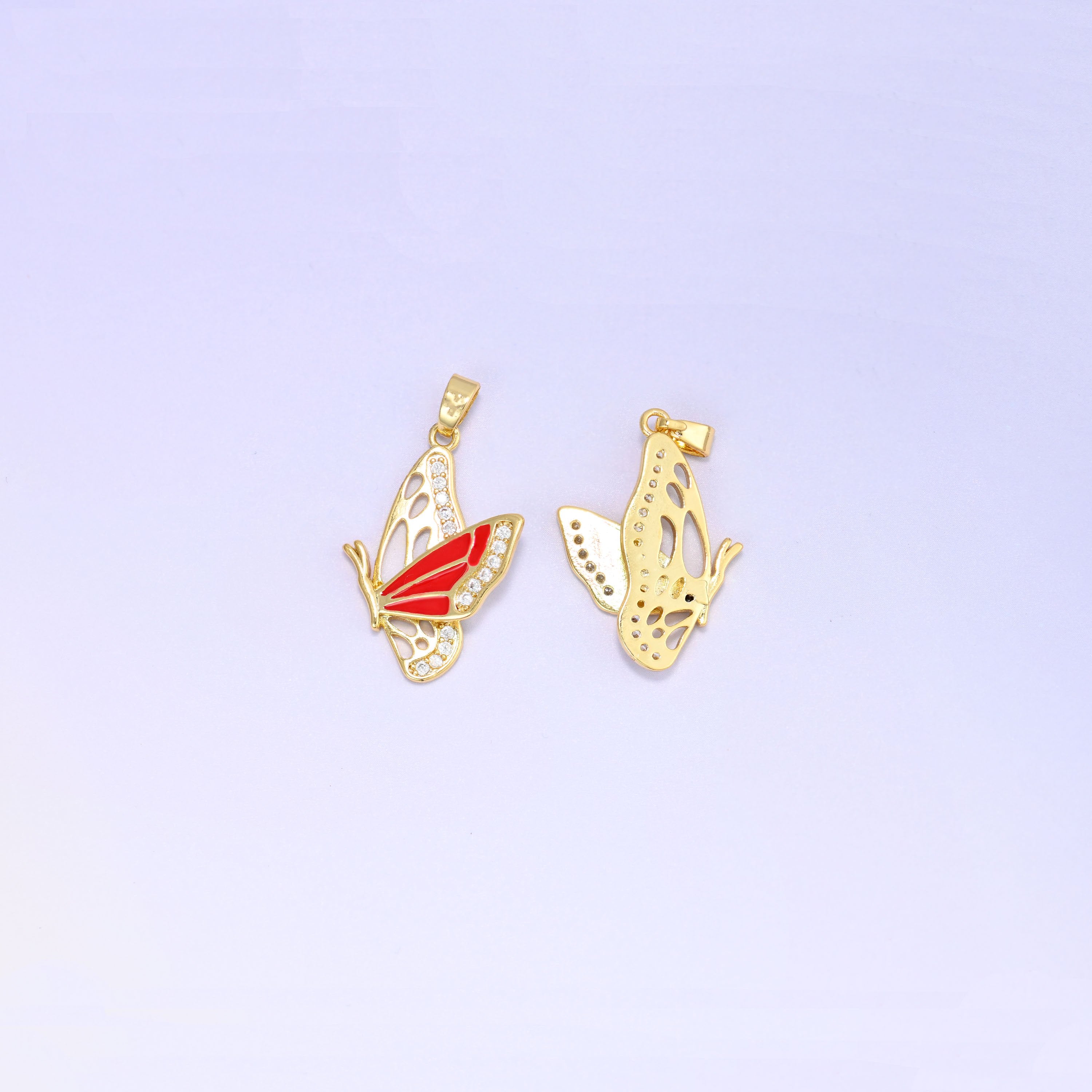 Flying butterfly charm pendant front and back, the red enamel and zirconia face beside the open filigree gold reverse of a second charm.