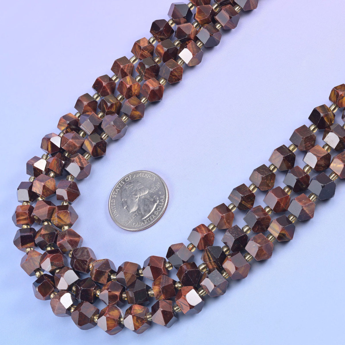 Faceted 8 sides diamond rhombus beads in dyed red tiger eye beside a US quarter laid flat for scale.