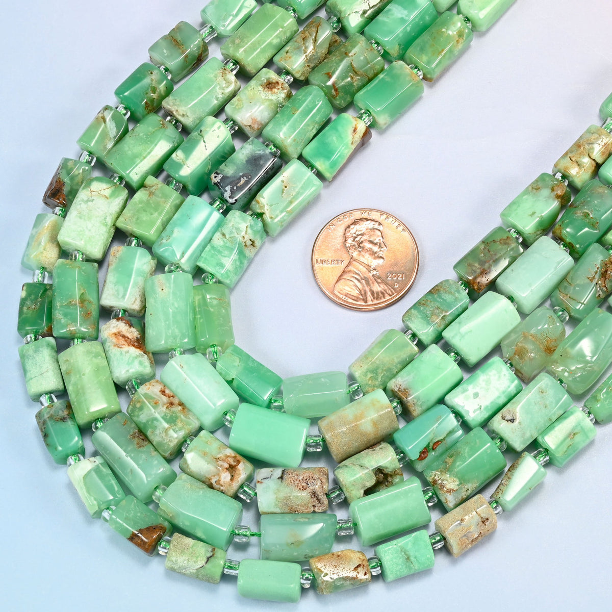 Close view of Australian jade faceted tube strands curving beside a US penny for scale
