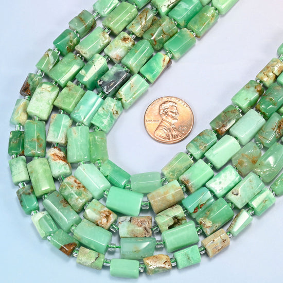 Close view of Australian jade faceted tube strands curving beside a US penny for scale
