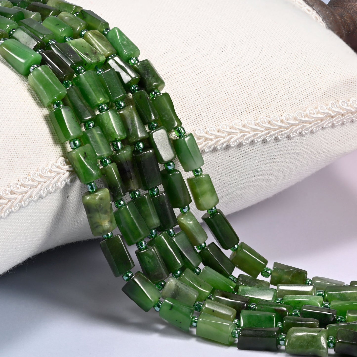 Canadian Green Jade faceted tube beads draped in rows, deep forest green tubes marbled with pale sage and cream white, spaced with small green glass seed beads
