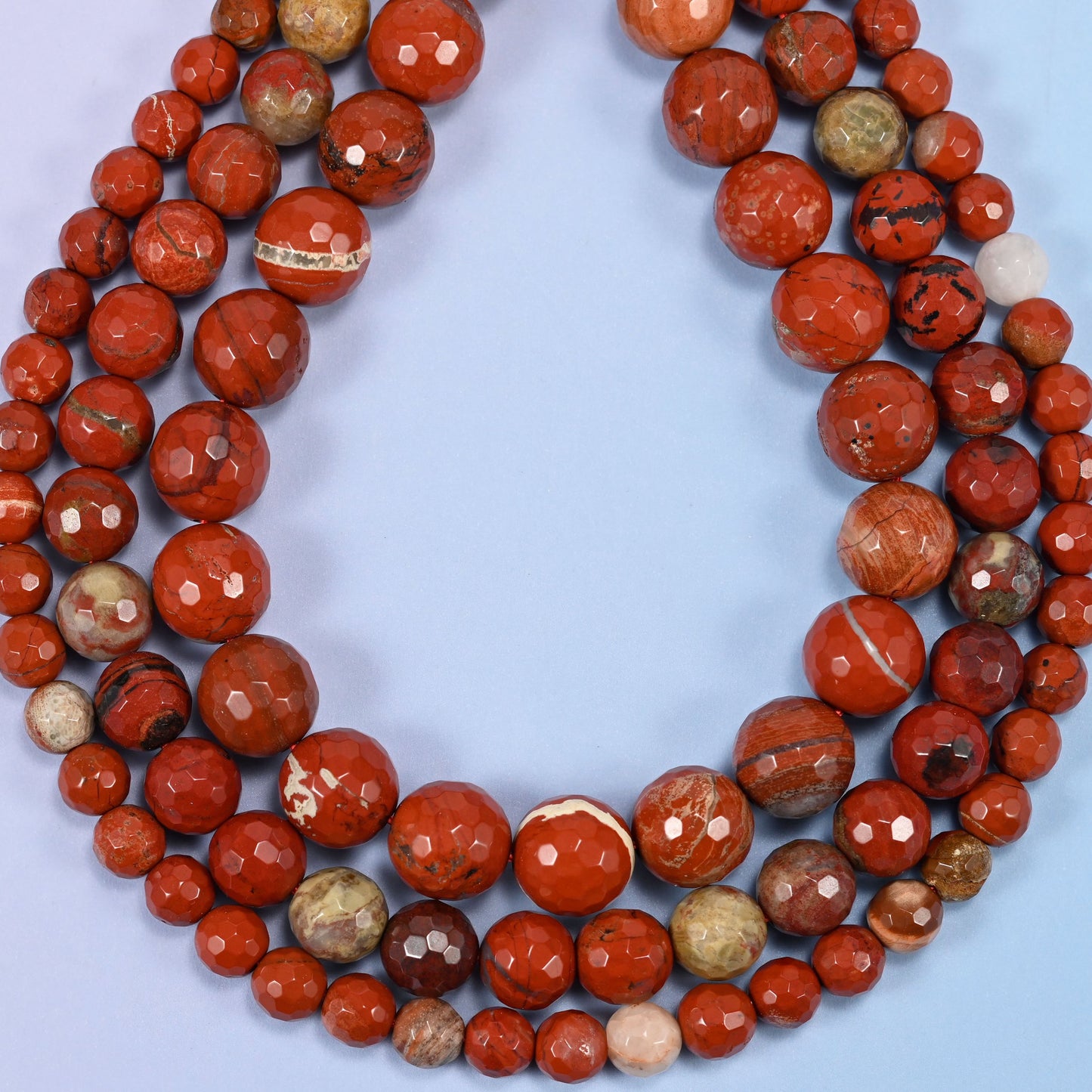 Close-up of a dense circular coil of red jasper faceted round beads, showing the facet cuts and stone patterning.