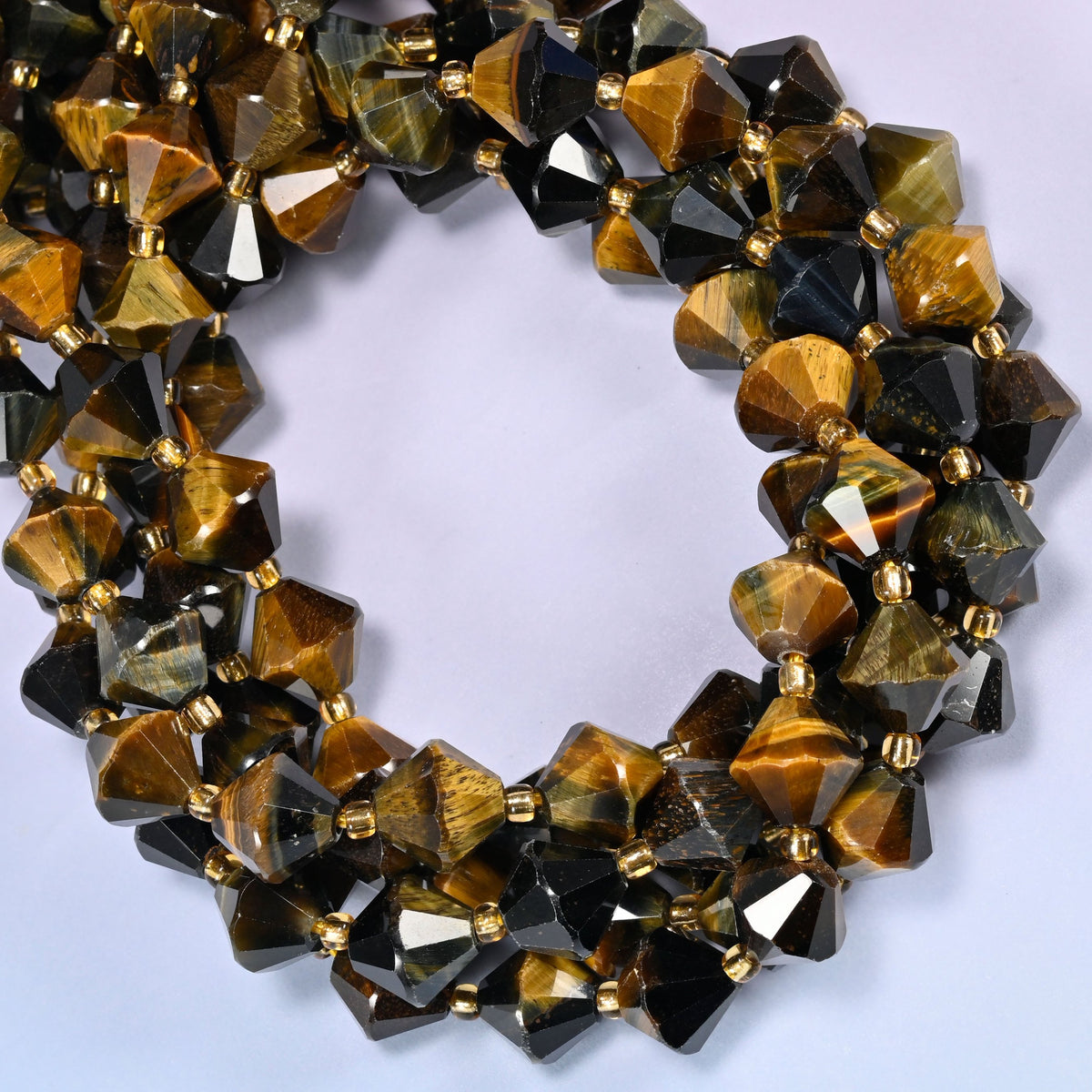10mm Iron Tiger Eye faceted bicone beads coiled tightly into overlapping loops on a light lavender background.