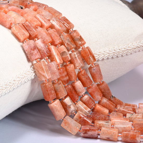 Close-up of multiple strands of faceted Golden Strawberry Quartz tube beads with clear glass spacer beads, draped over a cream fabric jewelry display bust.