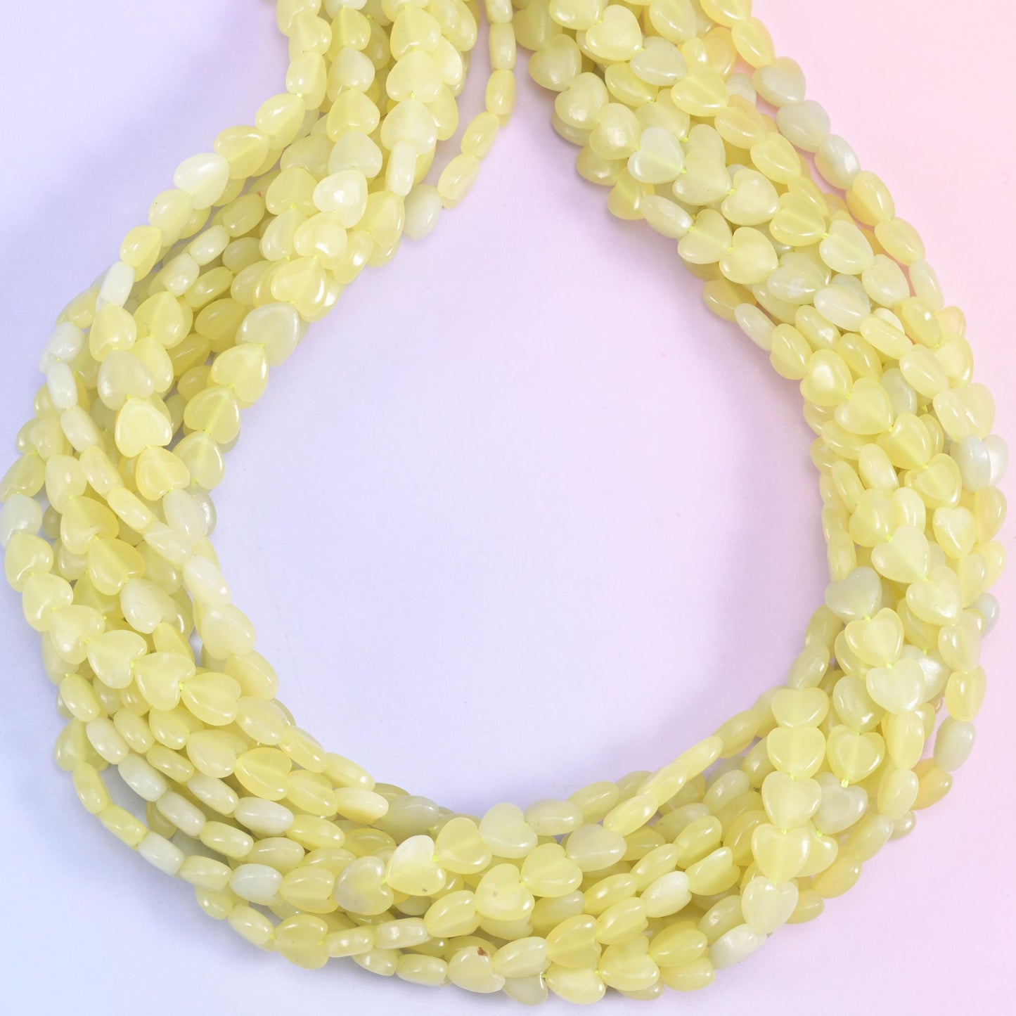 A soft buttery yellow stone, faintly translucent at the edges, with the odd pale grey and near-white heart scattered along the strand