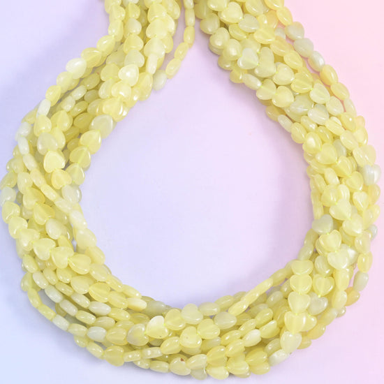 A soft buttery yellow stone, faintly translucent at the edges, with the odd pale grey and near-white heart scattered along the strand