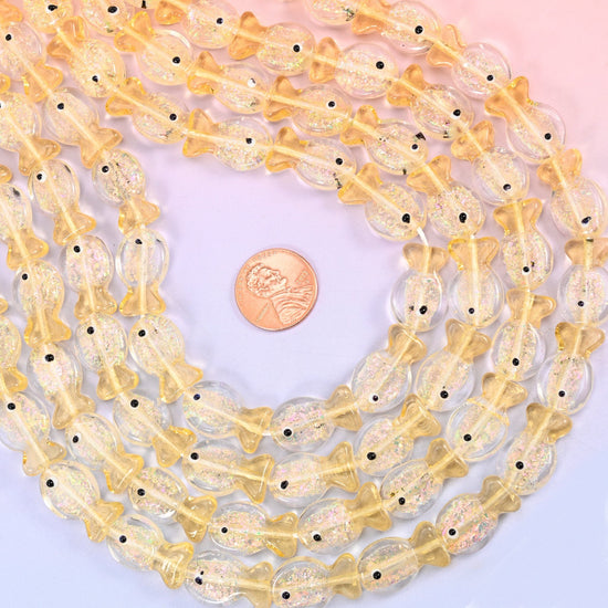 Iridescent Yellow Fish Glass Beads — little lampwork fish in clear butter-yellow glass with gold glitter suspended inside the body and a single black dot for the eye.