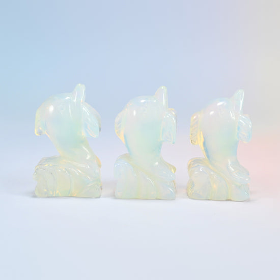 Three glowing opalite dolphin carvings turned at an angle