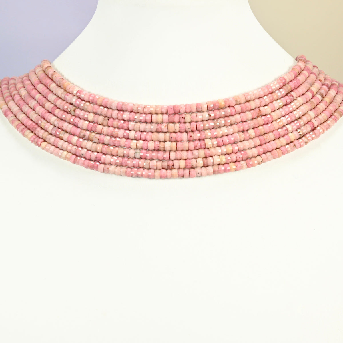 Pink rhodonite faceted heishi disc strands arranged as a layered collar on a white display bust, pink beads across the neck