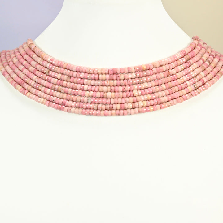 Pink rhodonite faceted heishi disc strands arranged as a layered collar on a white display bust, pink beads across the neck