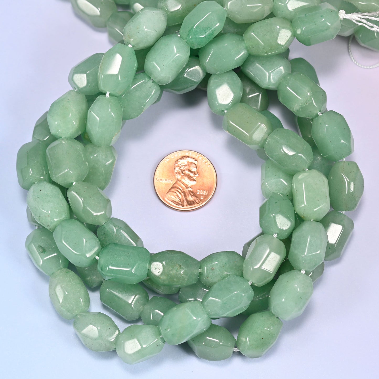 Close-up horizontal row of green faceted Aventurine barrel beads laid straight, showing the polished facet detail up close.