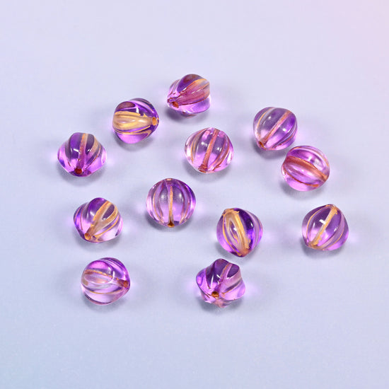 A scattered group of loose 8mm purple gold pumpkin glass beads, showing the melon ribs and the drill holes.