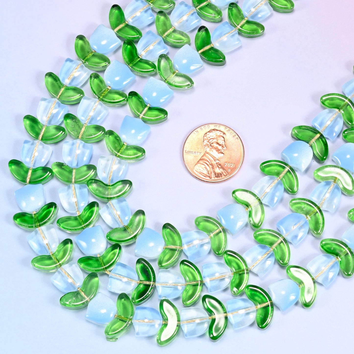 Wide circular coil of light blue tulip and green leaf glass bead strands forming a full wreath shape on a lavender and pink gradient background.