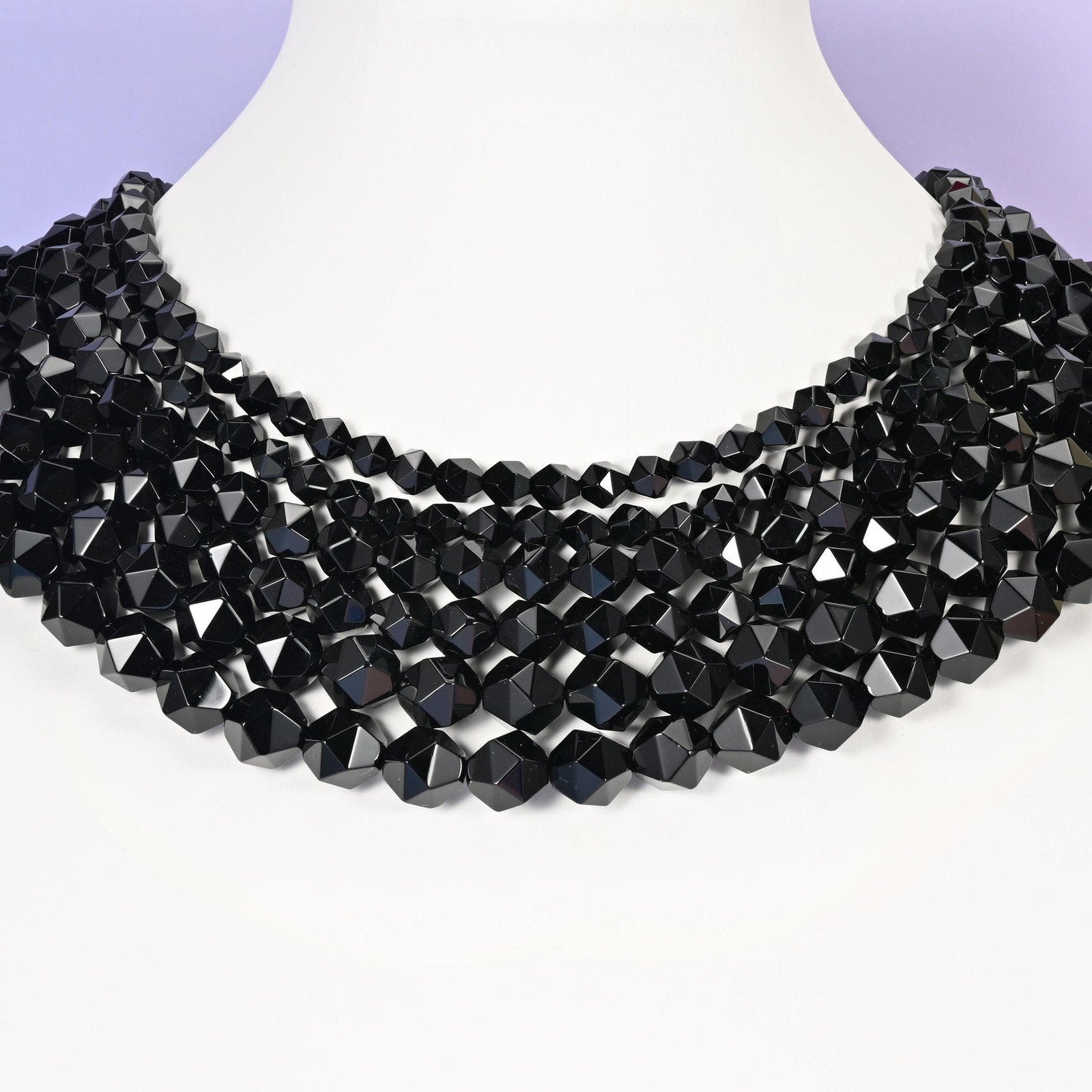 Black Onyx star cut beads looped around a white neck form, several strands sitting together as a collar