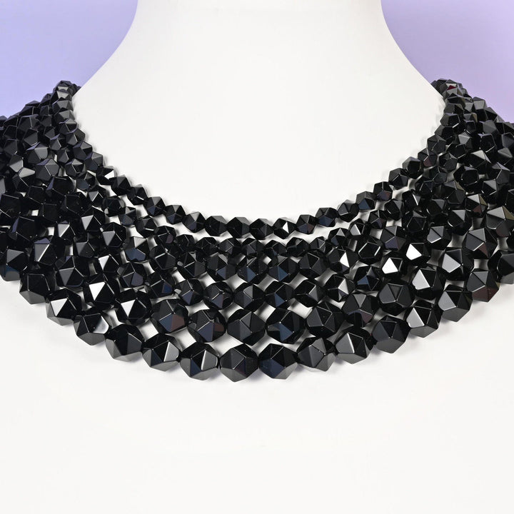 Black Onyx star cut beads looped around a white neck form, several strands sitting together as a collar