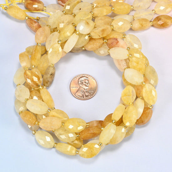 Golden healer quartz faceted flat oval beads 9x14mm coiled in a loop around a US penny for scale, close-up of the faceted flat oval shape