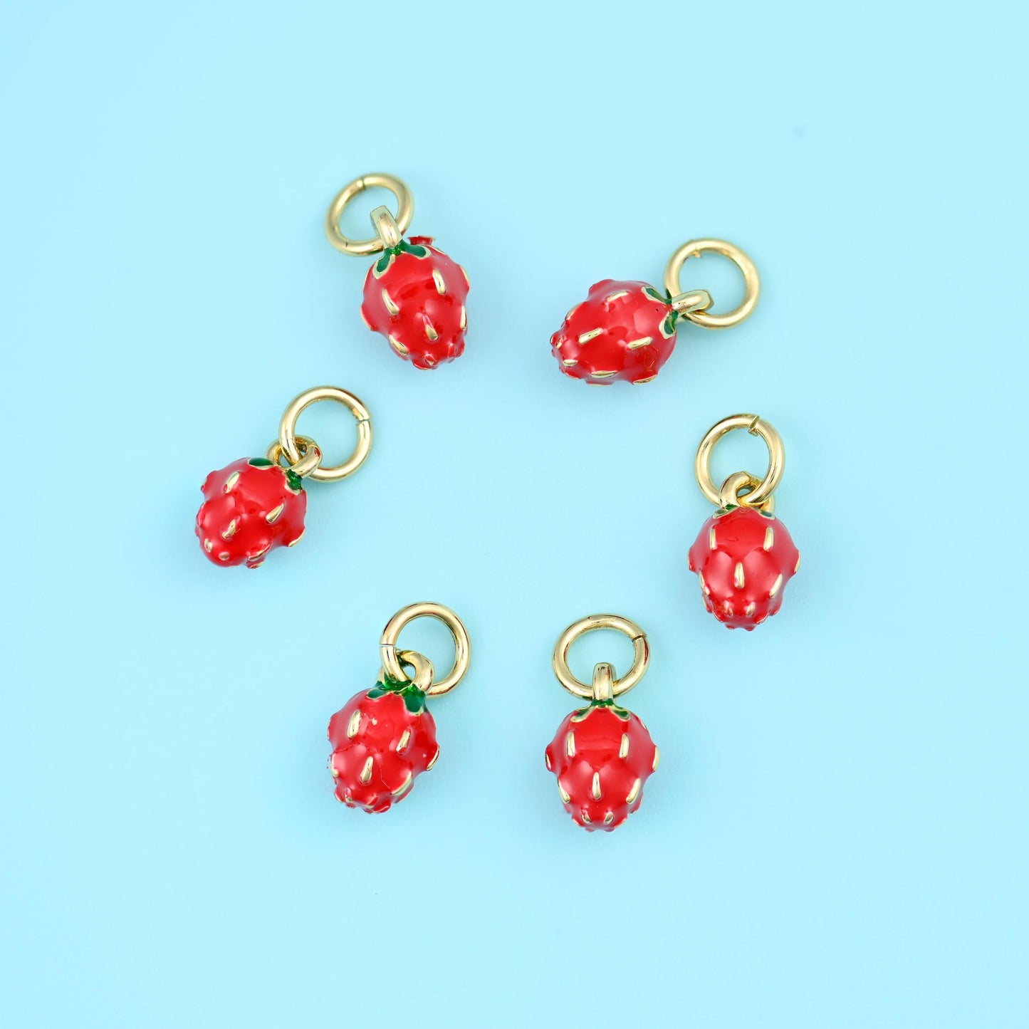 A miniature berry in glossy red enamel with a dimpled, seeded surface, a small green enamel leaf cap and a gold-tone ring…