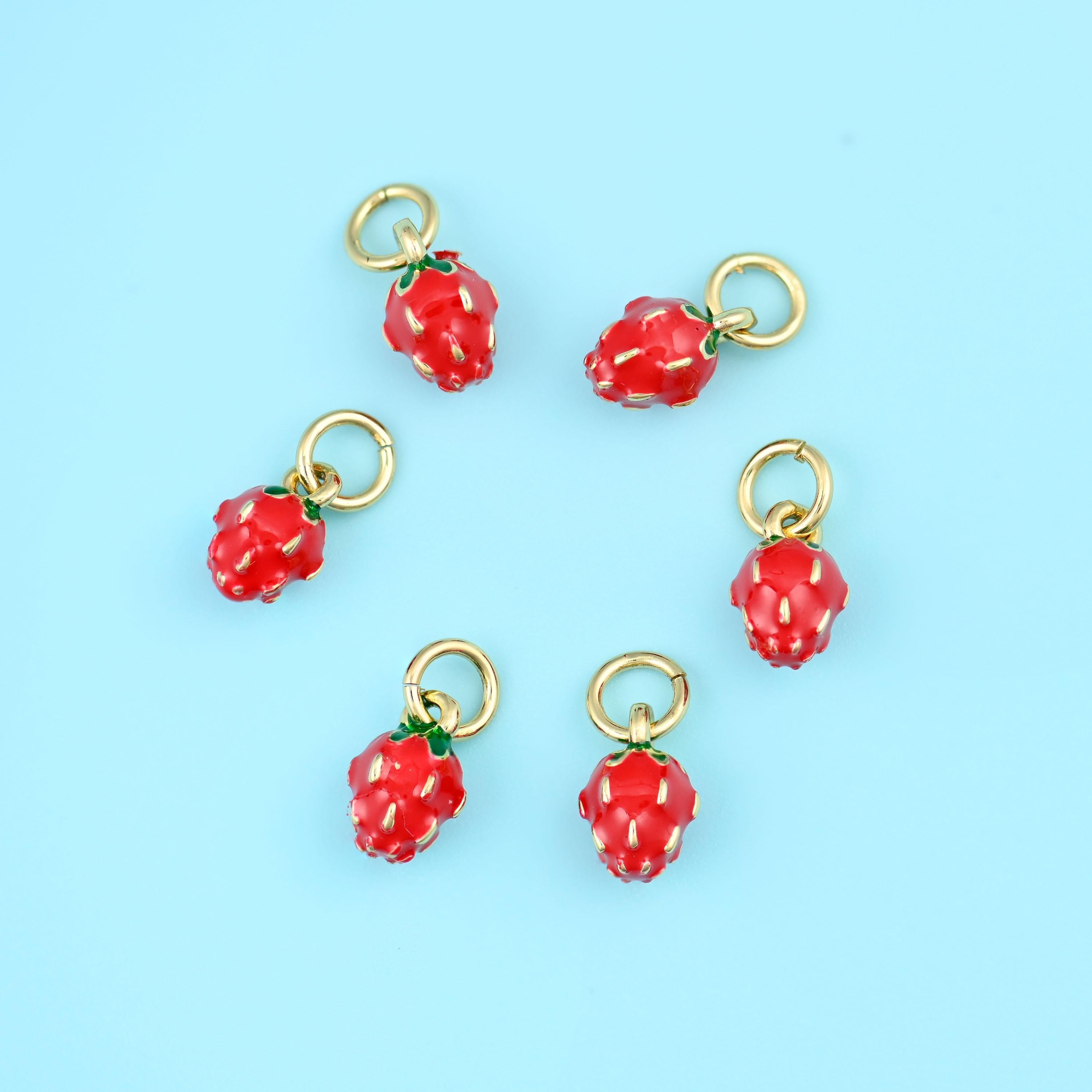 A miniature berry in glossy red enamel with a dimpled, seeded surface, a small green enamel leaf cap and a gold-tone ring…