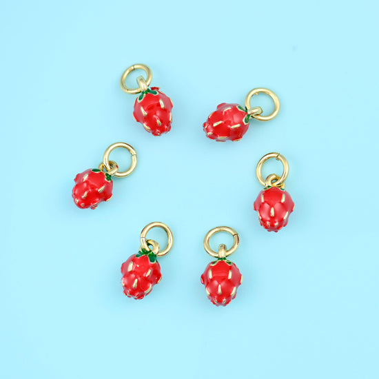 A miniature berry in glossy red enamel with a dimpled, seeded surface, a small green enamel leaf cap and a gold-tone ring…