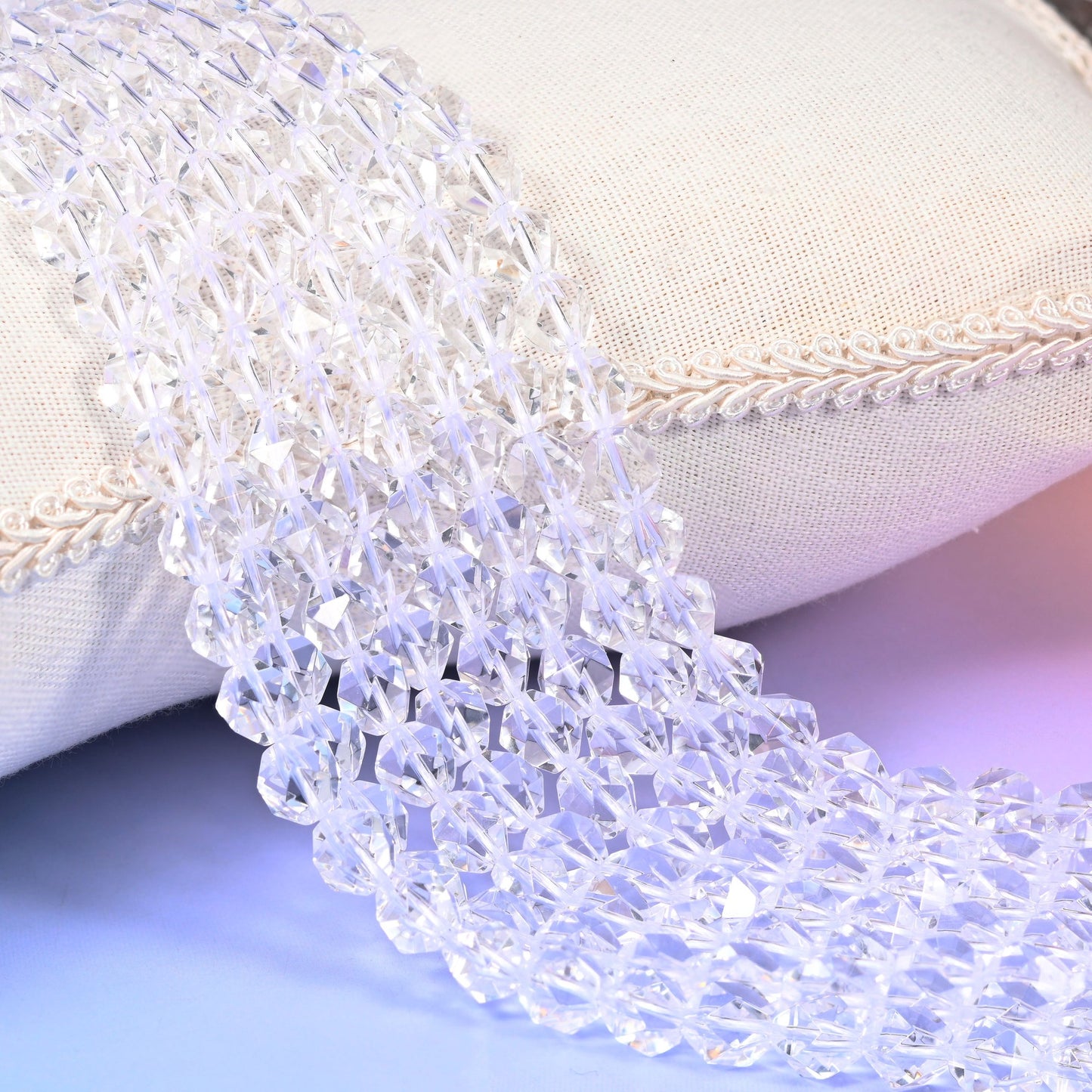 Clear Quartz diamond star cut beads, faceted transparent rounds, strands draped over a white cloth