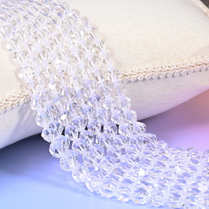Clear Quartz diamond star cut beads, faceted transparent rounds, strands draped over a white cloth