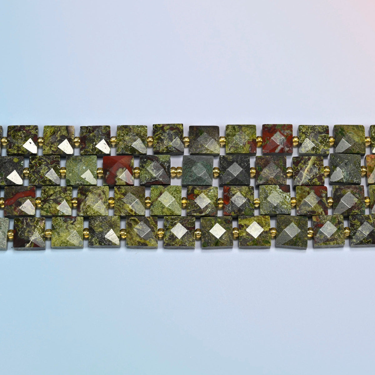 Several strands of natural dragon blood stone faceted flat square beads laid in straight rows