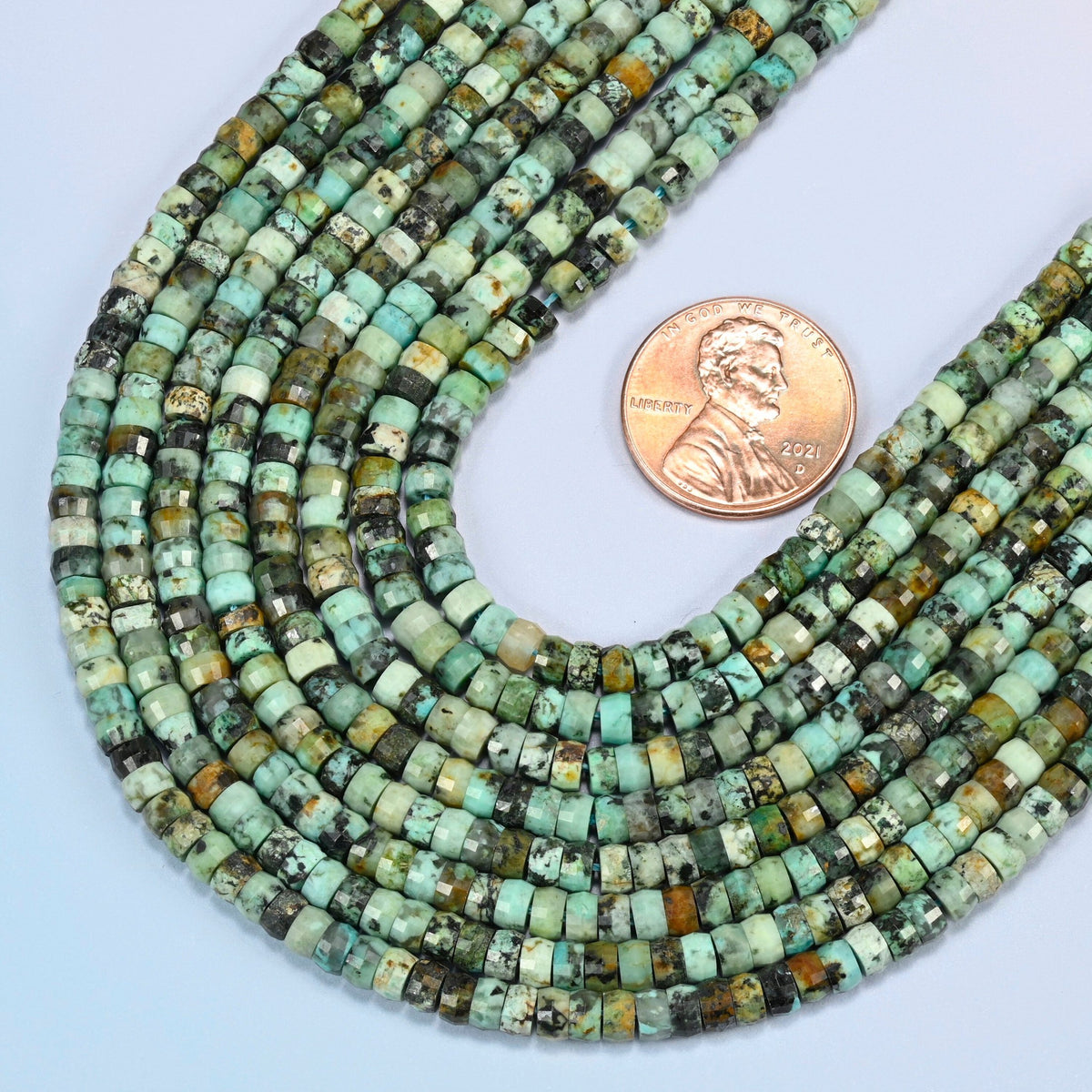 Close view of African howlite faceted heishi disc strands curving beside a US penny for scale