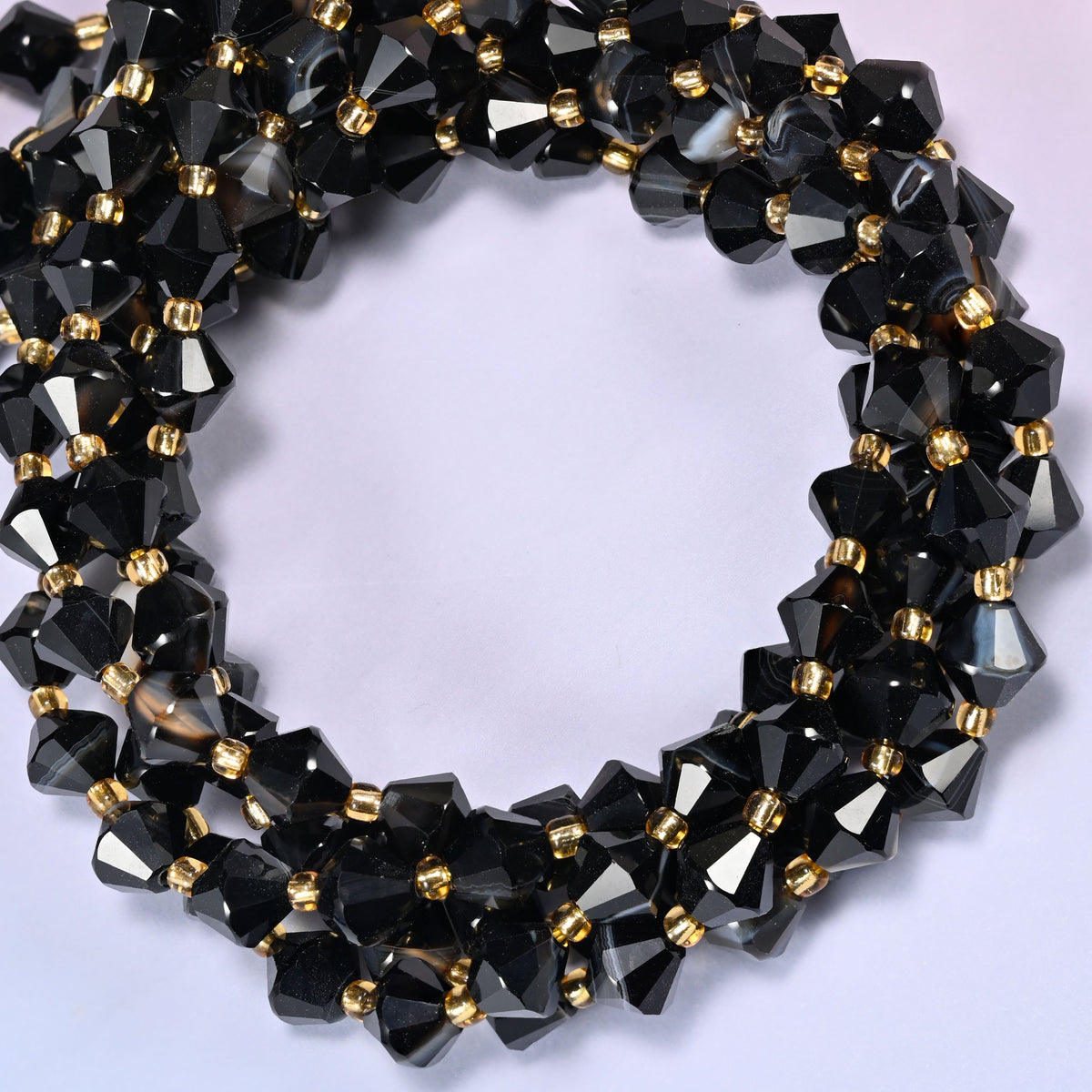 Dyed black strip agate bicone beads coiled into a round ring of several strands, bright white highlights breaking up the black along the curve.
