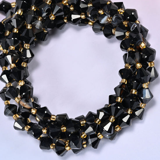 Dyed black strip agate bicone beads coiled into a round ring of several strands, bright white highlights breaking up the black along the curve.