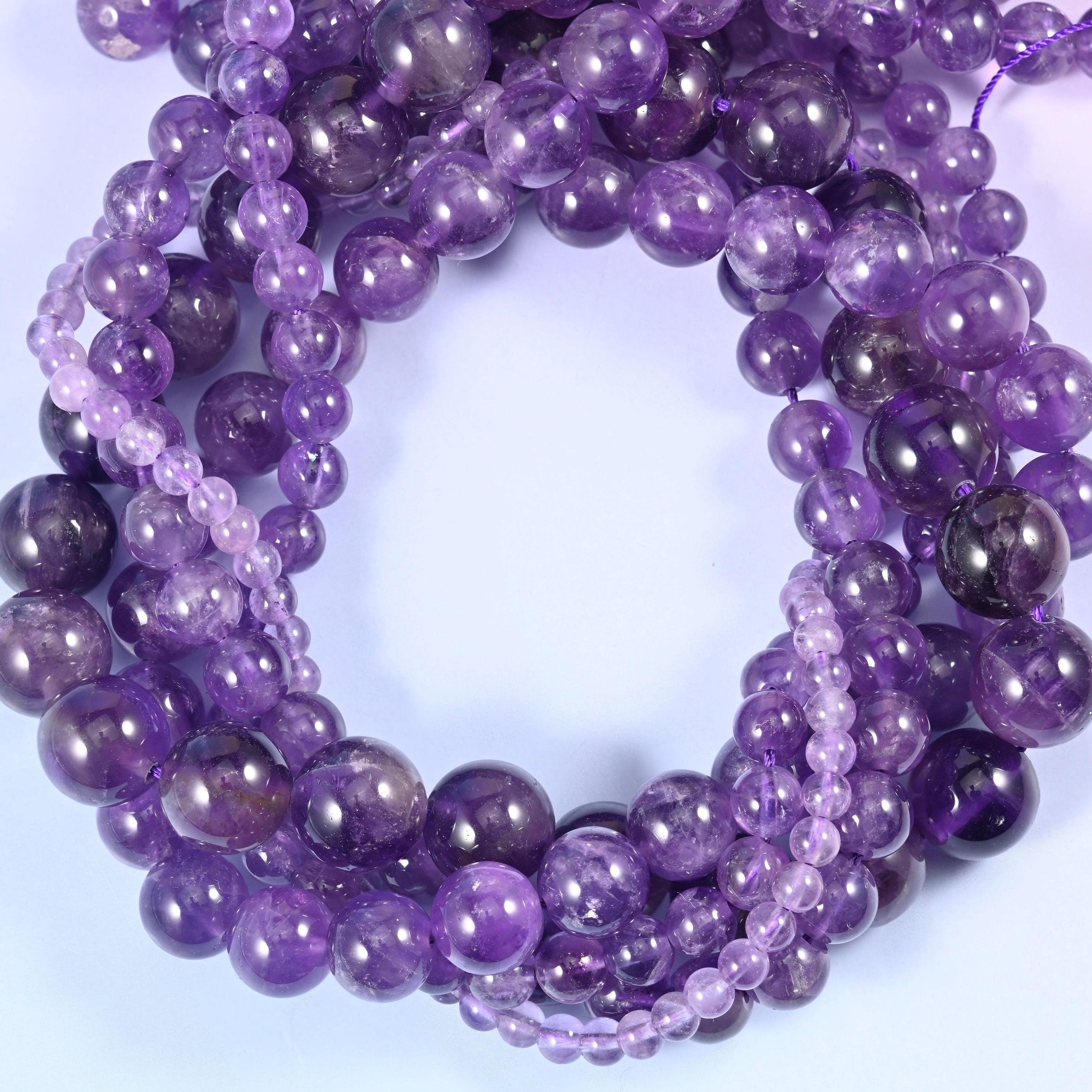 Translucent amethyst rounds that run from pale lilac to deep grape within the same strand, some beads veiled with milky white quartz, every one polished to a clean glassy shine.
