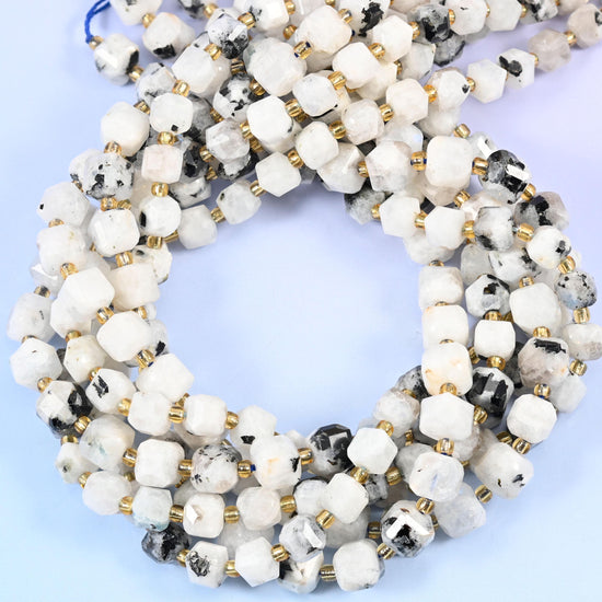 Milky white cubes blotched and flecked with charcoal black, corners cut into facets so light breaks across the flat faces. Despite the Blue Moonstone name these read white and grey in hand, not blue.