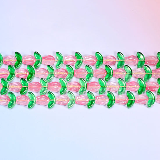 Overhead view of rows of pink tulip flower beads alternating with green leaf beads laid flat on a lavender surface.