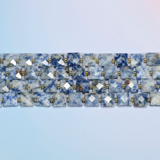 Several strands of natural blue spot jasper faceted flat square beads laid in straight rows