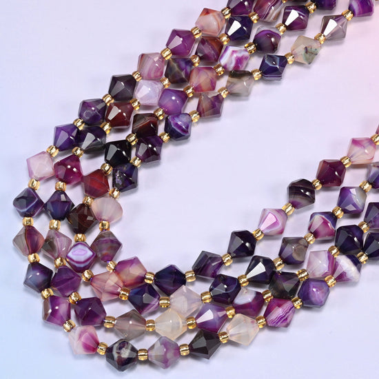 8mm Dyed Purple Strip Agate faceted bicone beads arranged in a loose curved strand on a light lavender background.