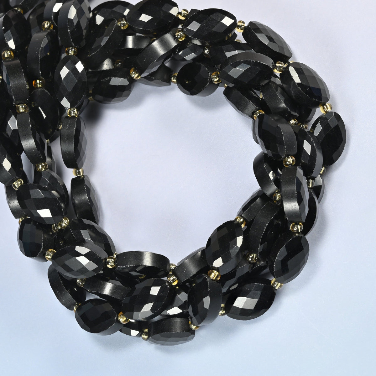 Black onyx faceted flat oval beads coiled into overlapping loops, whole strands of solid black stone