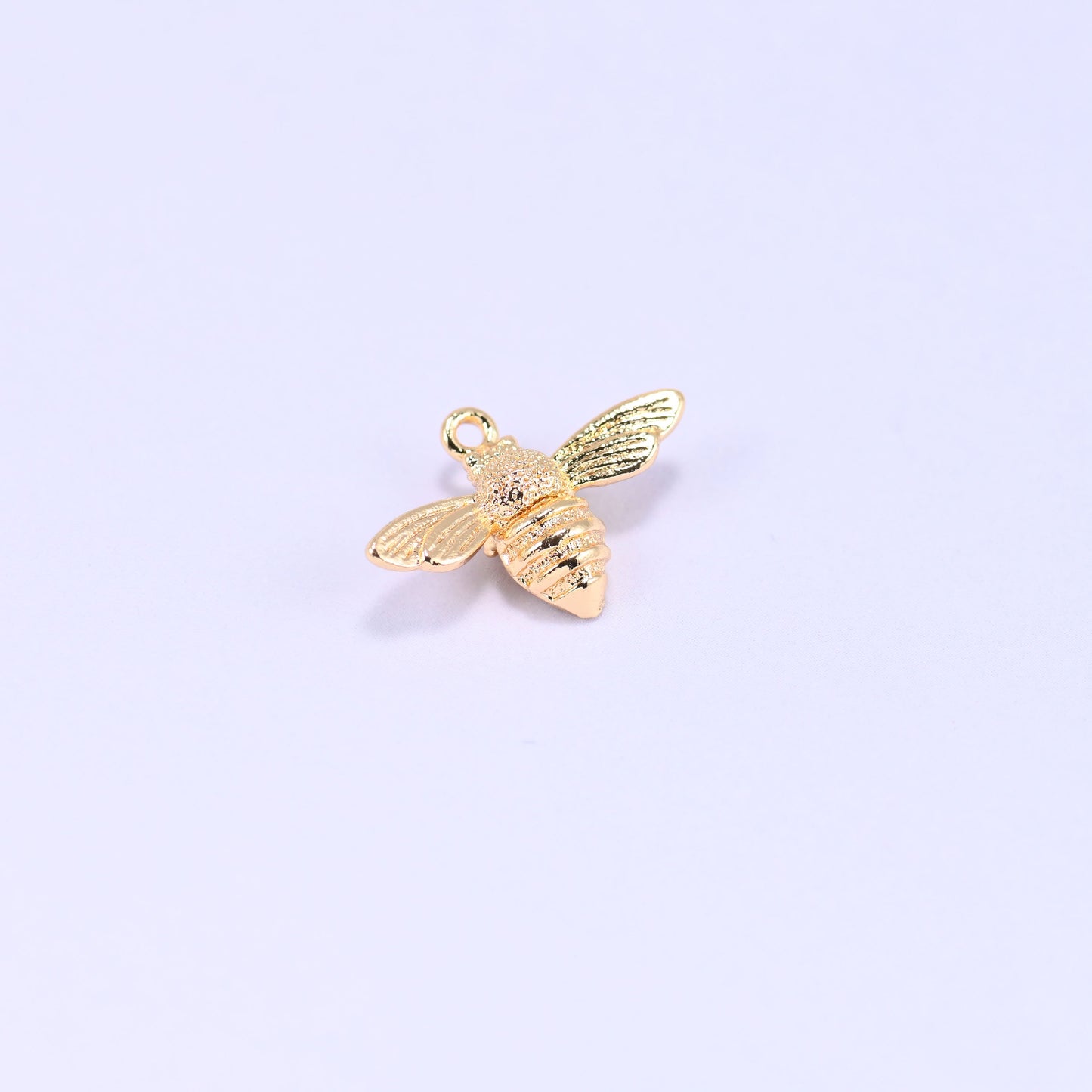 Small gold charms bee, single charm at an angle showing the stippled thorax and ribbed body