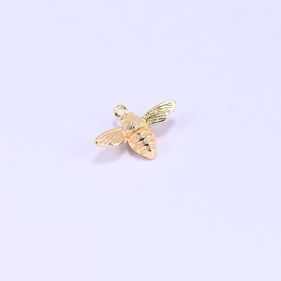 Small gold charms bee, single charm at an angle showing the stippled thorax and ribbed body